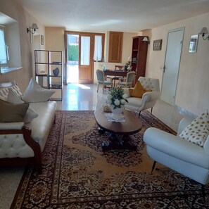 Amplia sala de estar con alfombra grande, sofás blancos, una mesa de centro y un comedor con sillas y mesa.