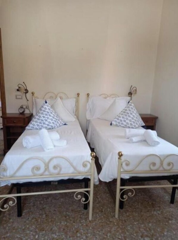 Two single beds with white linens and patterned pillows, each with a small bedside table and a lamp. - Near the center (Lucca)