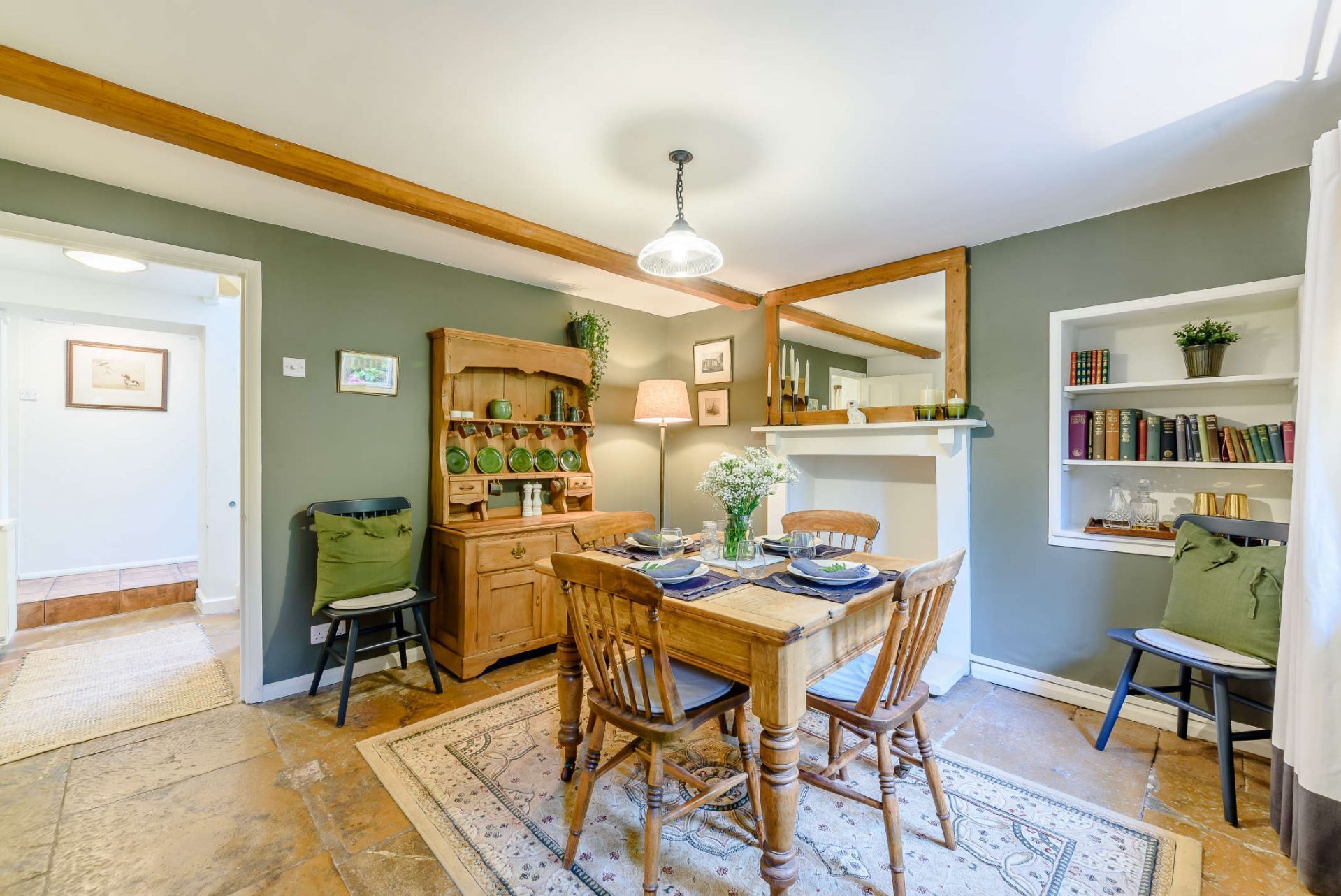 A dining area with a wooden table, chairs, a rug, a cabinet with dishes, and a bookshelf with books.