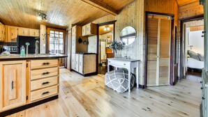 A wooden cabin interior with a kitchen area, wooden cabinets, a sink, and a dining table.