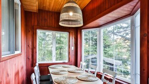 A wooden dining room with a large table, white chairs, and a woven pendant light.