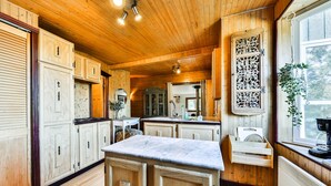 A wooden interior with a kitchen area featuring cabinets, a marble countertop, and a window with a plant.