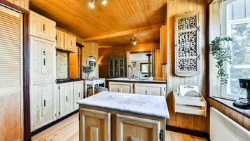 A wooden interior with a kitchen area featuring cabinets, a marble countertop, and a window with a plant.