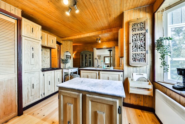 A wooden interior with a kitchen area featuring cabinets, a marble countertop, and a window with a plant.