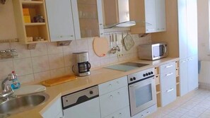 Una cocina con armarios blancos, microondas, cafetera y pileta.