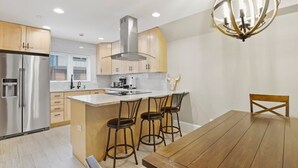 Una cucina moderna con isola centrale, elettrodomestici in acciaio inossidabile e un tavolo da pranzo in legno con sgabelli da bar.
