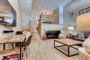Un salón amplio con chimenea, una mesa de comedor y una escalera que sube a un nivel superior.