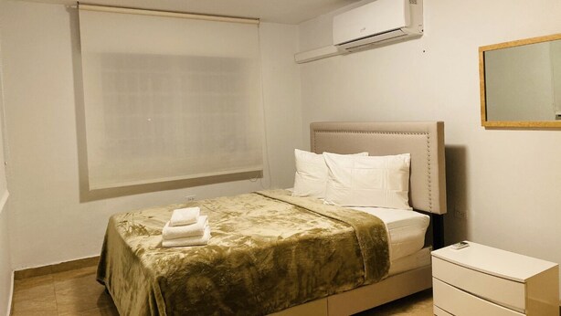 A bedroom with a bed, a nightstand, a dresser, a window with blinds, and an air conditioning unit. - New Beautiful 2 bedroom full Apartment San Juan, Area Metro. (San Juan)