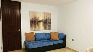 A room with a dark wooden door, a blue sofa with patterned cushions, and a cityscape painting on the wall. - New Beautiful 2 bedroom full Apartment San Juan, Area Metro. (San Juan)