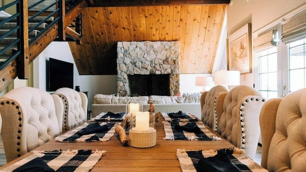 A cozy living room with a stone fireplace, plush armchairs, a wooden coffee table, and a staircase. - Private beach, boat slip, hot tub, pool table, fenced yard, BBQ, fire pit (Bass Lake)