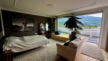 Un dormitorio con cama, sofá, un ventanal y vista a un paisaje montañoso.