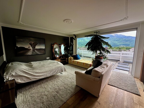 A bedroom with a bed, a sofa, a large window, and a view of a mountain landscape.
