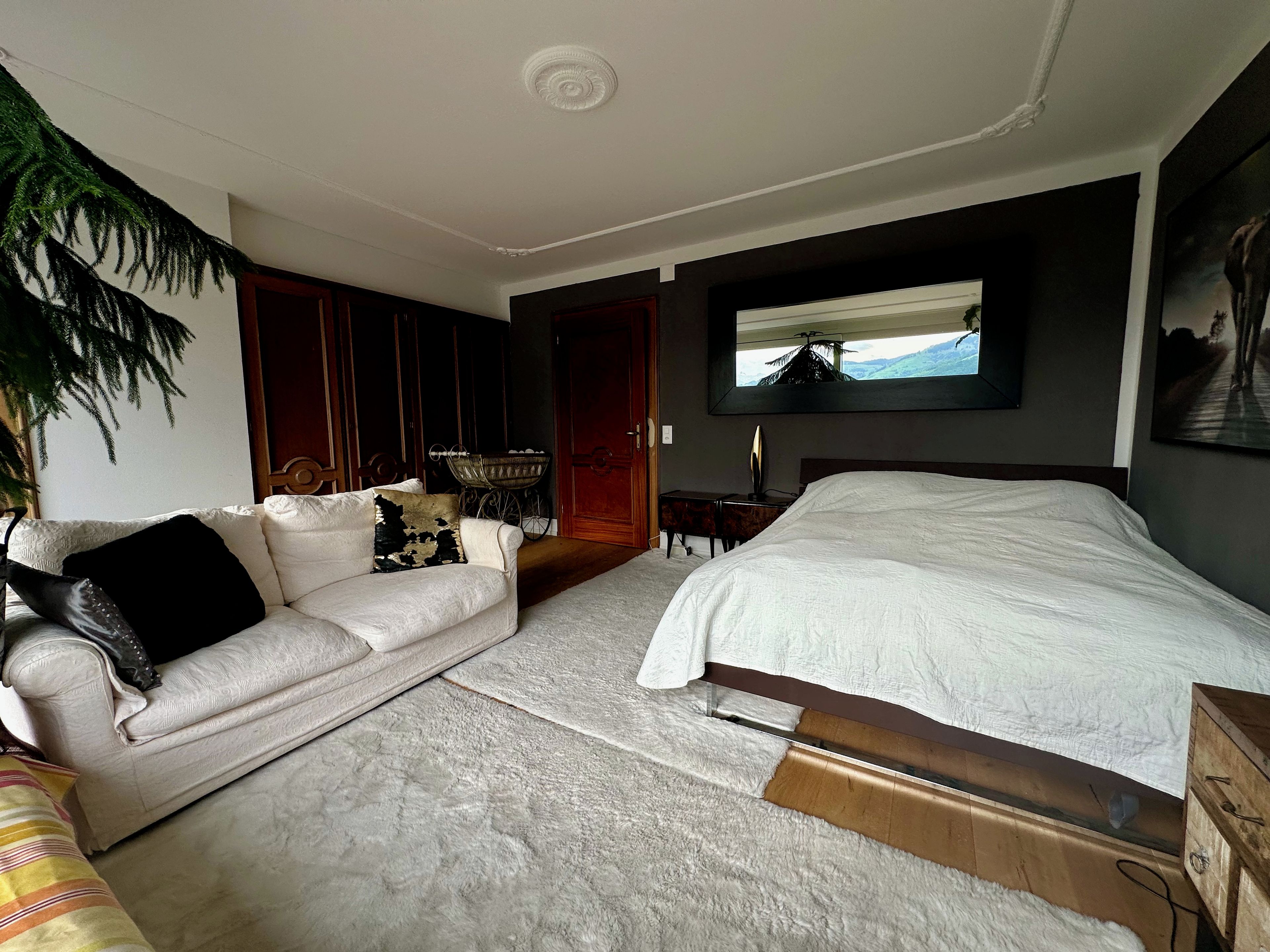 Ein Schlafzimmer mit einem Bett, einer Couch, einem Fernseher und einem großen Fenster.