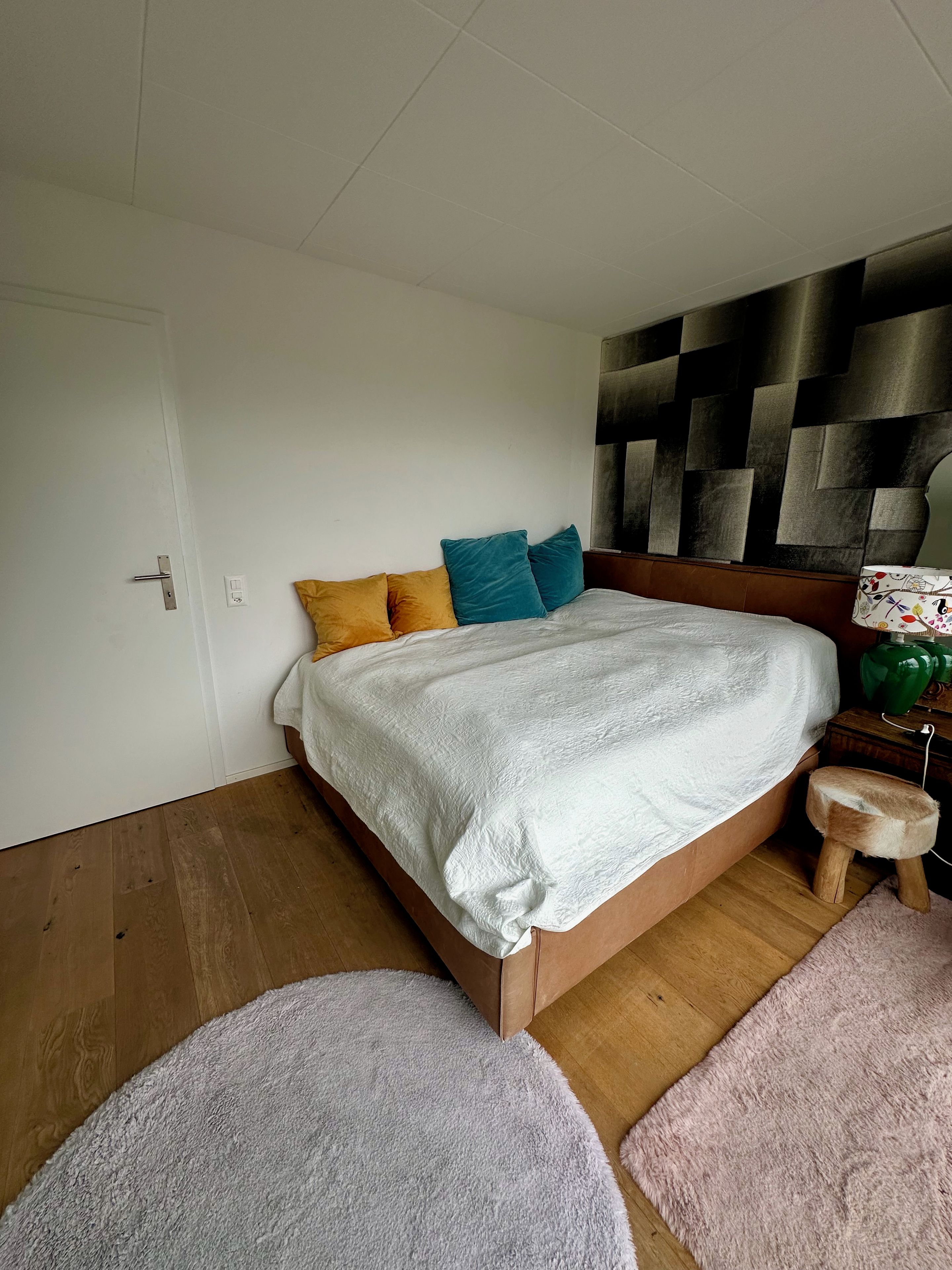 Un dormitorio con una cama de madera, una manta blanca y un cabecero con diseño geométrico.