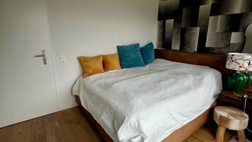 Un dormitorio con una cama de madera, una manta blanca y un cabecero con diseño geométrico.