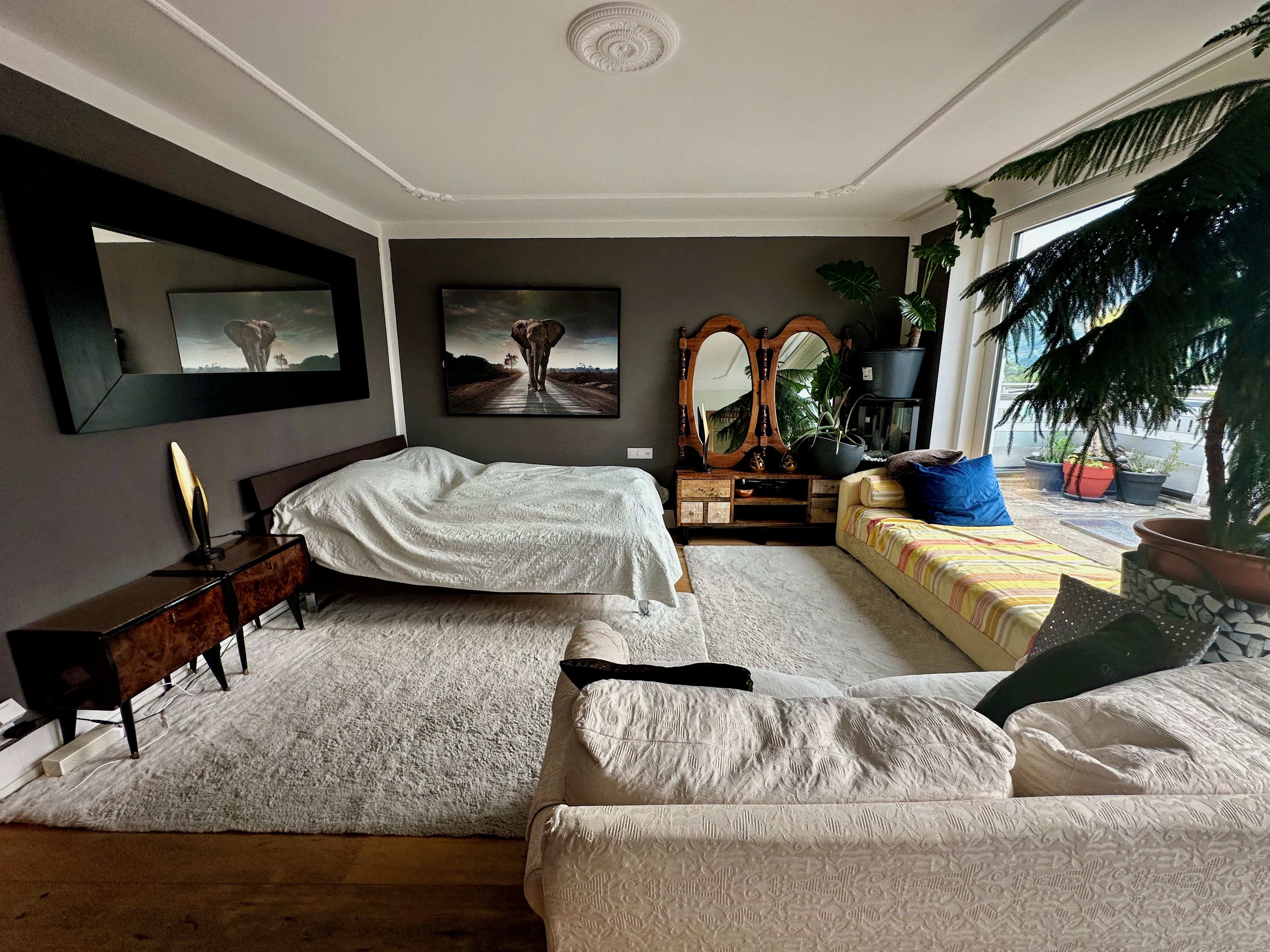Ein Schlafzimmer mit zwei Betten, einem Schminktisch, einem Spiegel und einem Fenster mit Pflanzen.