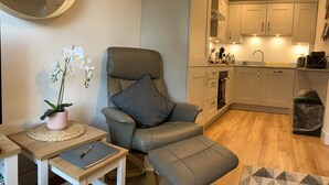 A modern living room with a leather armchair, a small table with a notebook, a potted orchid, and a geometric rug. - A stroll to Ringwood, near to New Forest & South Coast Beaches. Private Parking (Ringwood)
