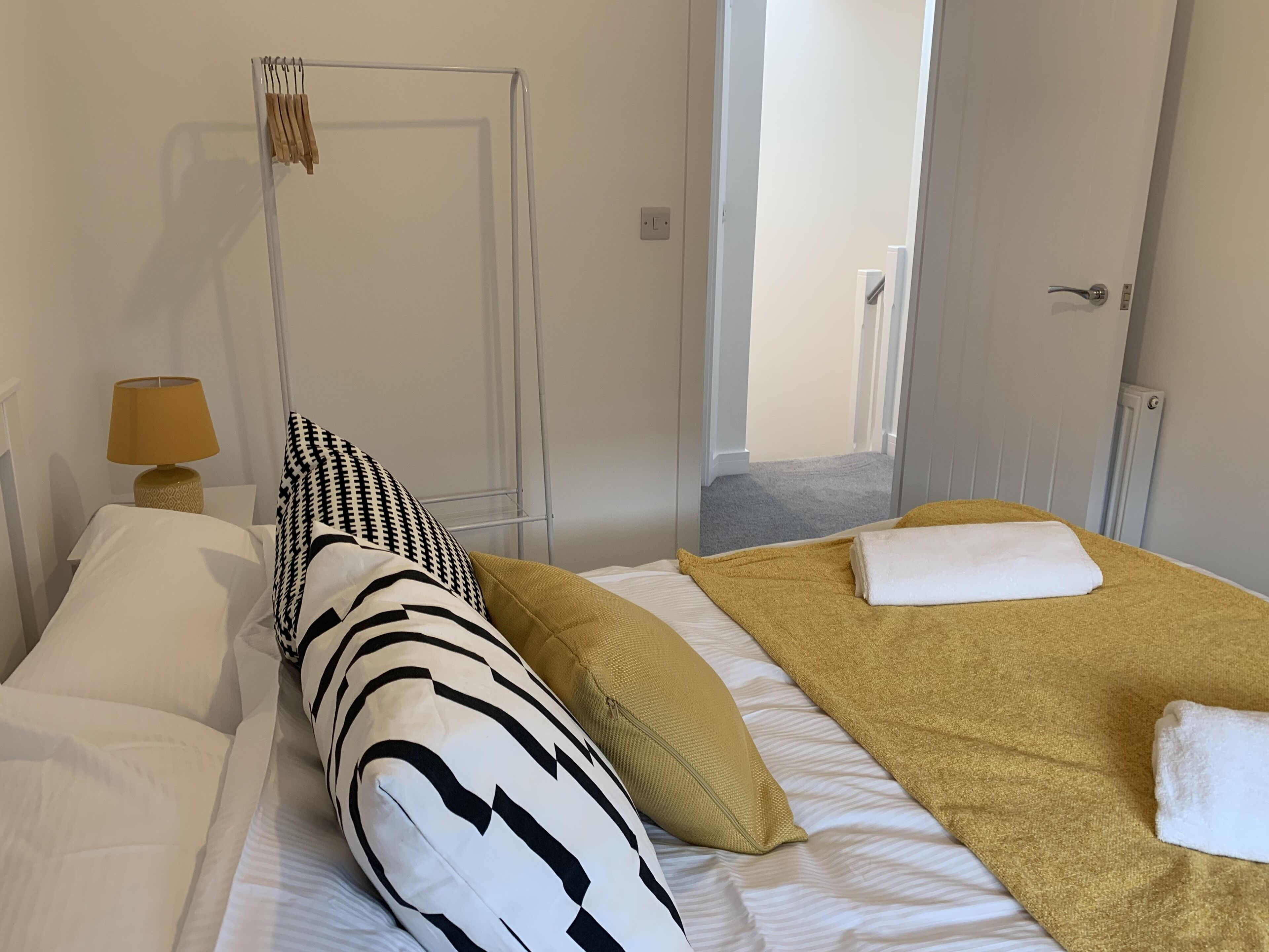 Habitación de hotel con cama, lámpara de noche, puerta y vista al pasillo.