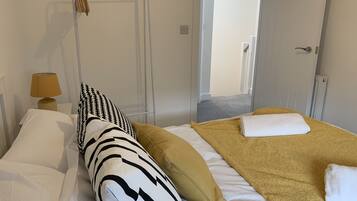 Habitación de hotel con cama, lámpara de noche, puerta y vista al pasillo.