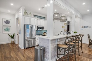 A modern kitchen with white cabinetry, stainless steel appliances, and a marble island with bar stools.