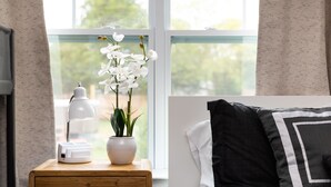 A bedroom with a wooden nightstand, a white lamp, a potted plant, and a bed with black and white pillows.
