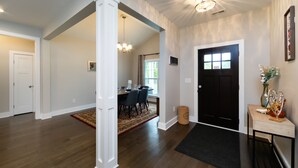 A spacious hallway with wooden flooring, a black door, and a dining area with chairs and a table.