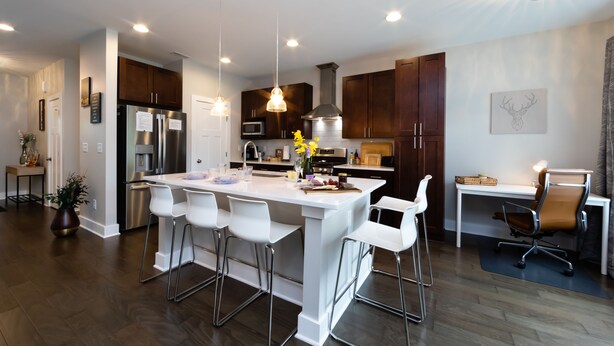 A modern kitchen with stainless steel appliances, a white island with bar stools, and pendant lighting.