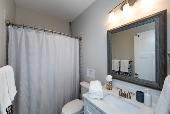 A bathroom with a shower curtain, toilet, sink with faucets, and a mirror.