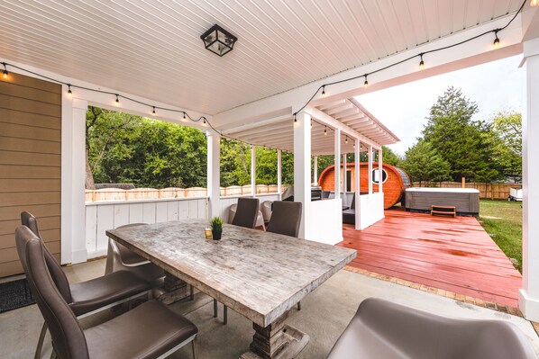 Un patio exterior con una mesa y sillas de madera, una zona de estar techada y un jacuzzi.