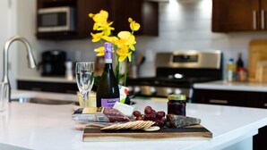 A kitchen counter with a cheese board, grapes, crackers, a bottle of olive oil, and a jar of jam.