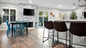 Une cuisine moderne avec un mur de crédence en pierre, un téléviseur à écran plat et un coin repas avec des chaises bleues.