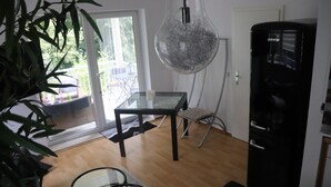 Une cuisine moderne avec un réfrigérateur noir, une table en verre et un luminaire suspendu.