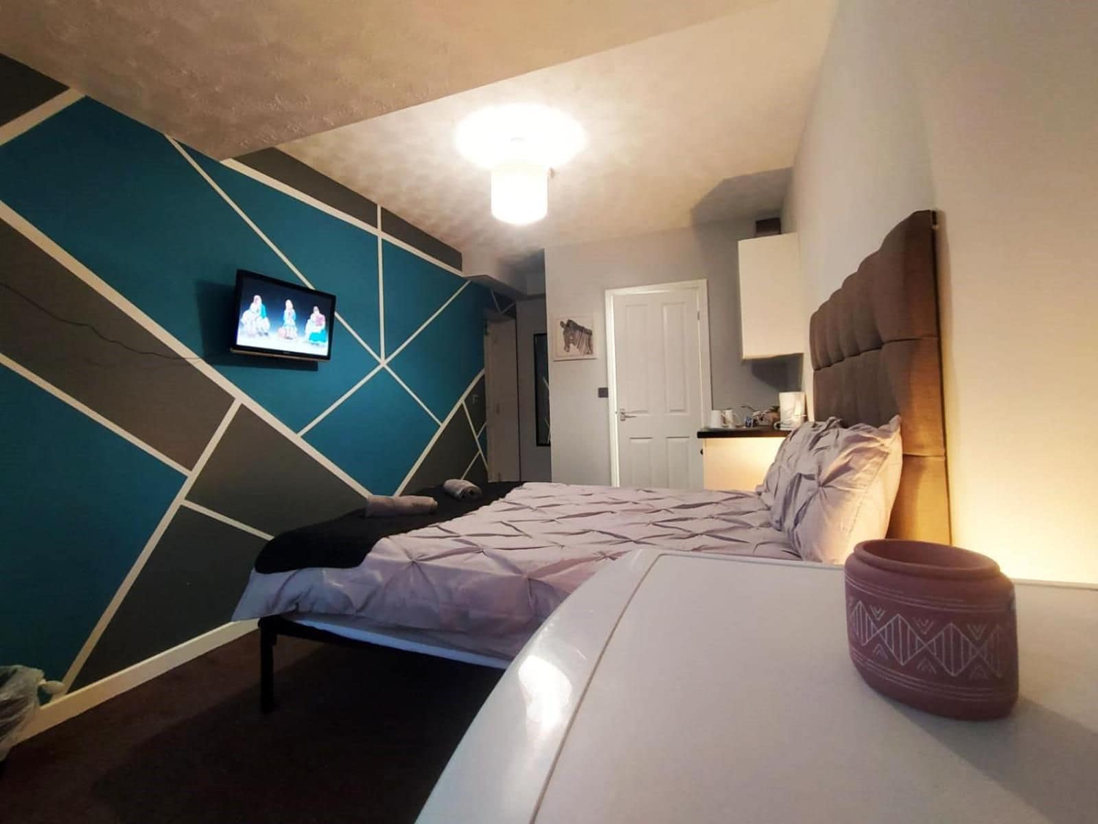 A bedroom with a bed, a television mounted on the wall, and a door leading to a kitchenette.