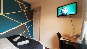 A hotel room with a bed, a desk, a chair, and a television mounted on the wall.