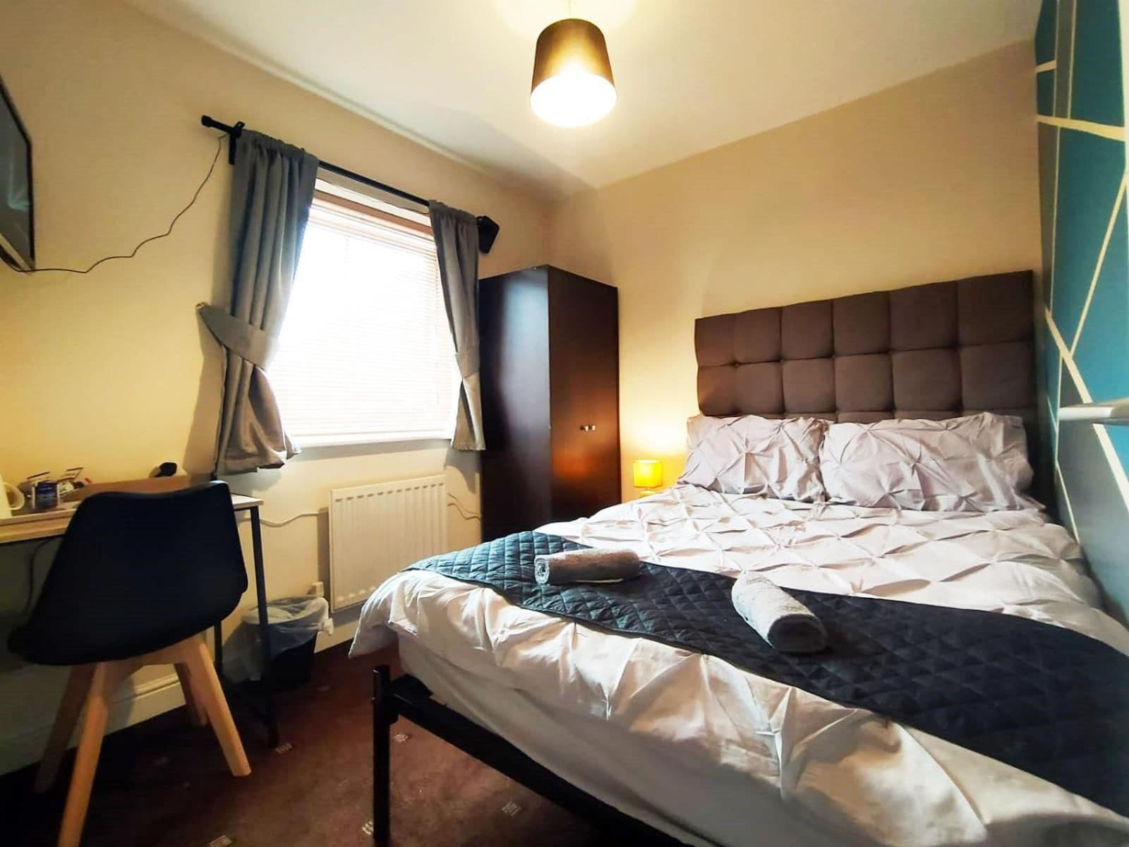 Een hotelkamer met een bed, een bureau, een stoel en een raam met gordijnen.