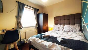 Een hotelkamer met een bed, een bureau, een stoel en een raam met gordijnen.