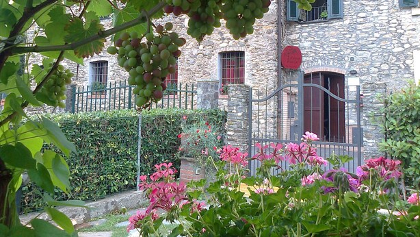 A stone building with a metal gate, a red door, and a sign with handwritten text. - The Tralcio, beautiful! (Garlenda)