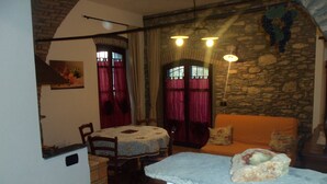 A cozy room with a stone wall, a round table with chairs, a sofa, and a small stone table. - The Tralcio, beautiful! (Garlenda)