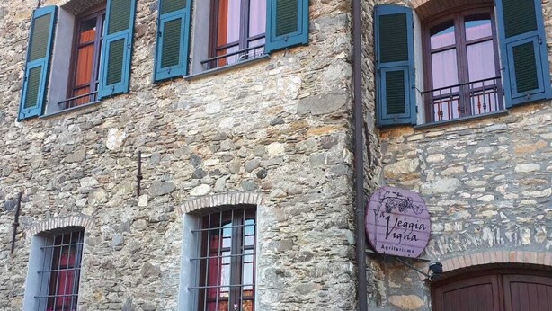Ein Steinhaus mit mehreren Fenstern, von denen einige mit Rollläden versehen sind, und einem Schild, das ein Restaurant namens „Veggia Vigna“ anzeigt.