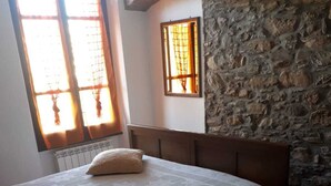 Ein Schlafzimmer mit einer Steinsäule, einem Bett mit weißer Bettdecke und zwei mit Vorhängen versehenen Fenstern.