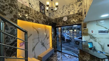 A lobby with marble flooring, a staircase, a reception desk, and a view of the street outside.