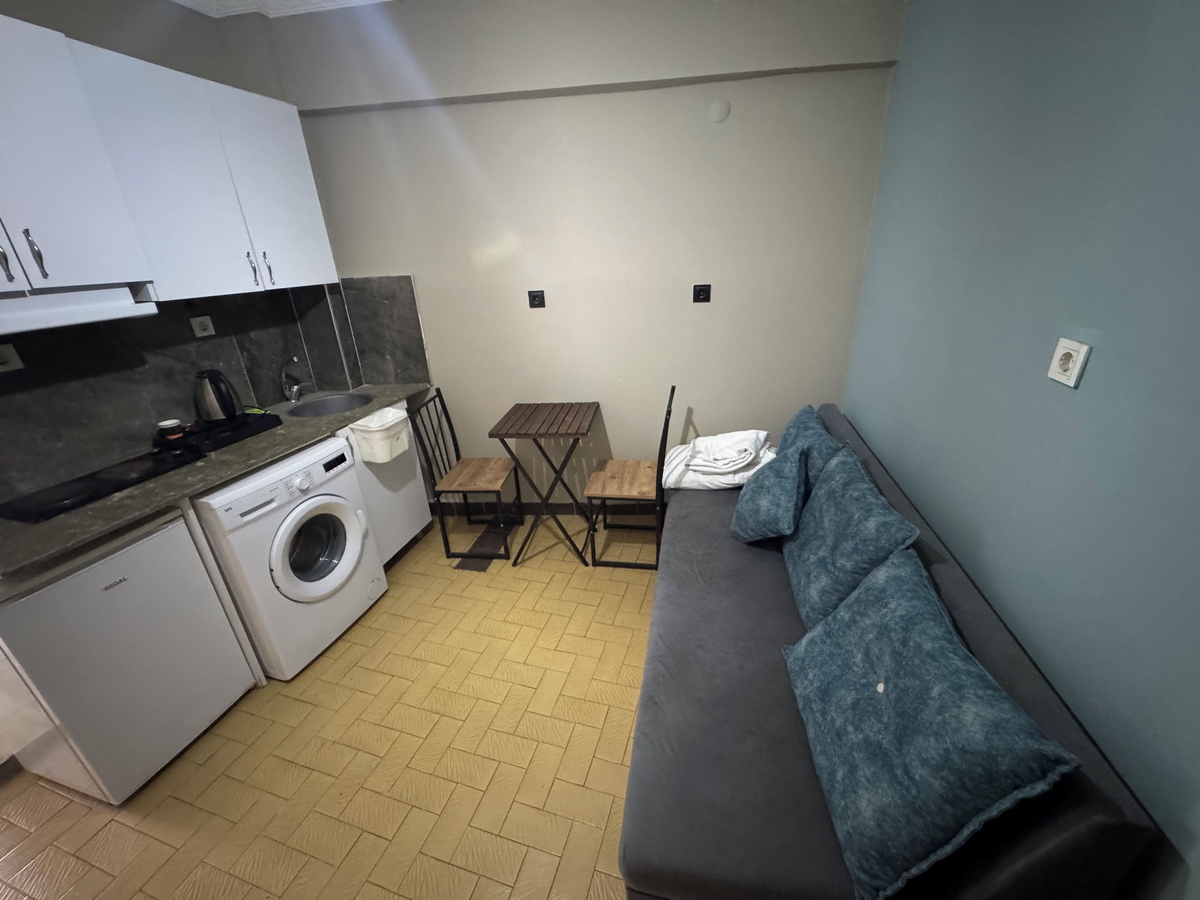 Un espacio habitable compacto con lavadora, una pequeña mesa, un sofá y una kitchenette.