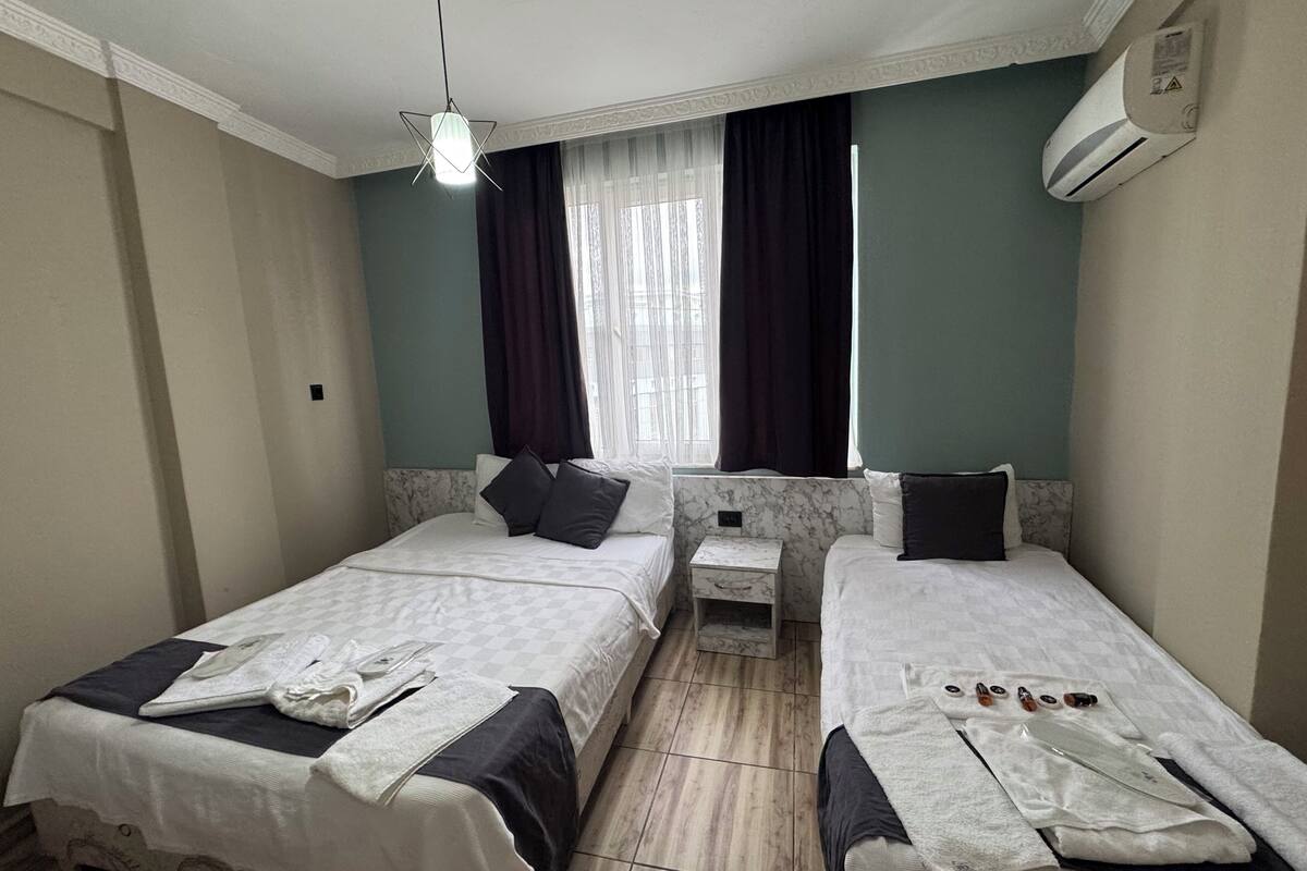 Une chambre d’hôtel avec deux lits, une petite table de chevet, une fenêtre avec des rideaux et un appareil de climatisation.