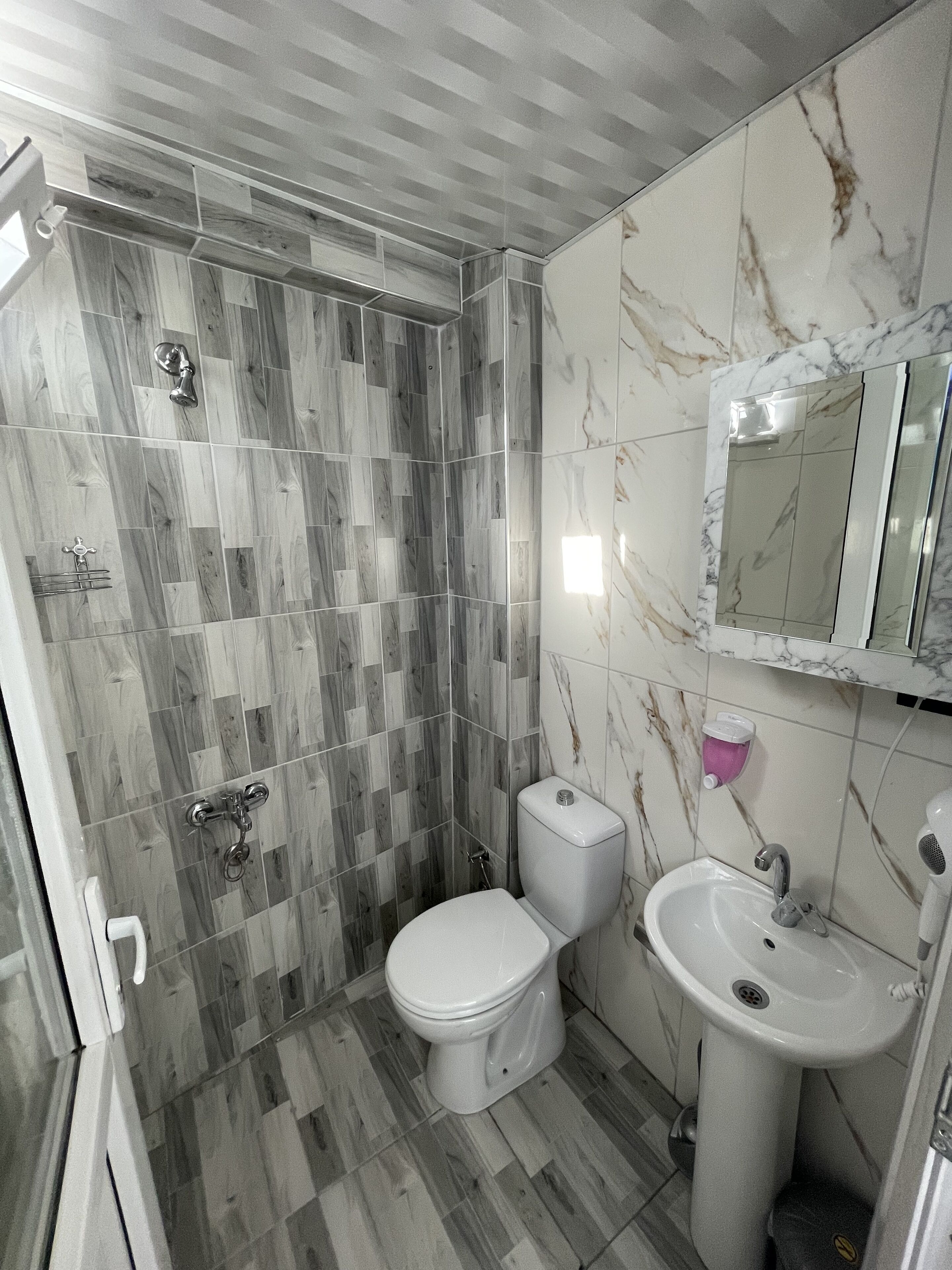 A bathroom with a shower, toilet, sink, and marble wall tiles.