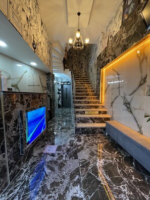 Un área de recepción con suelo de mármol, una televisión, una escalera y un mostrador de recepción.