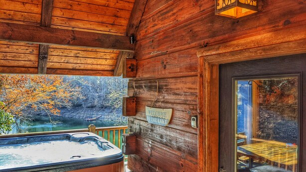 Una cabaña de madera con jacuzzi, un letrero de bienvenida y vistas al lago.