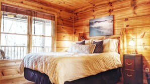 Un dormitorio de cabaña de madera con una cama, una mesita de noche, una lámpara y un cuadro en la pared.