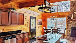 Interior de una cabaña de madera con cocina, comedor y chimenea de piedra.