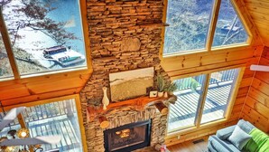 Interior acogedor de una cabaña con chimenea de piedra, paredes de madera, ventanas amplias y un comedor.