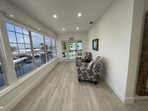 A spacious room with large windows overlooking a marina, a patterned sofa, and a door leading to an outdoor area.